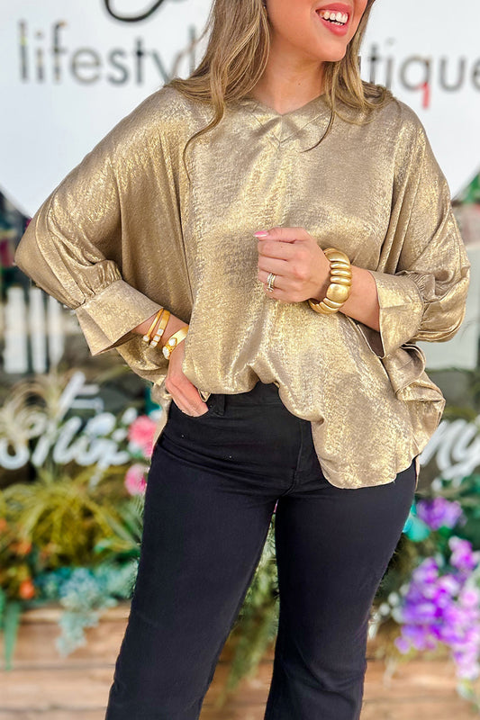 Blusa tipo dolman color pergamino metalizado con cuello en V, botones y puños en las mangas largas.