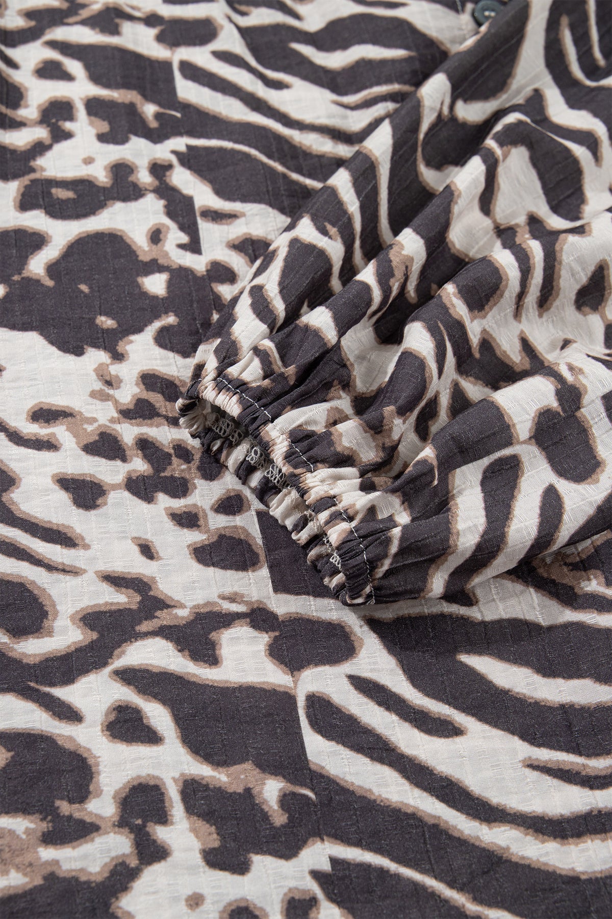 Camisa color pergamino con estampado de leopardo, cuello en V, cierre de botones y mangas abullonadas.