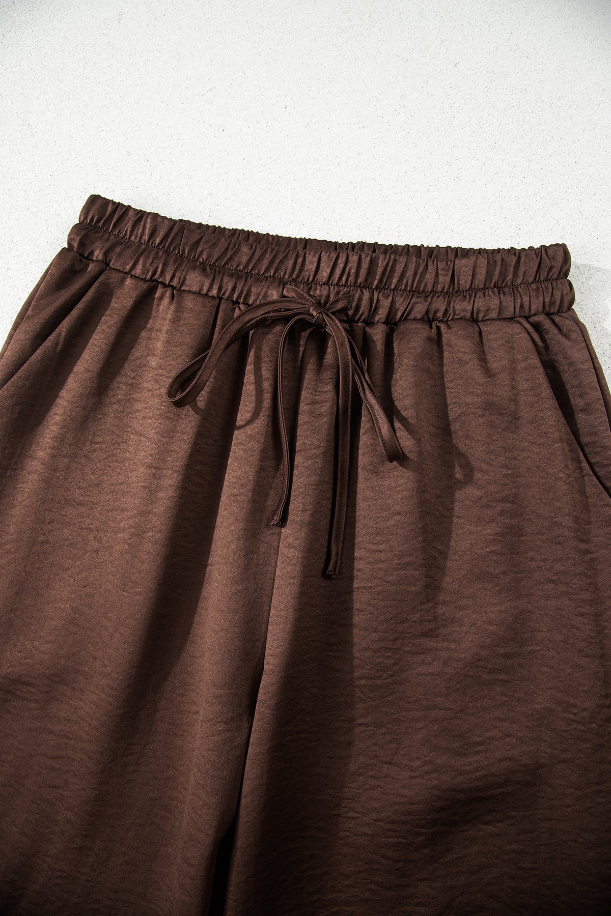 Conjunto de 2 piezas: blusa holgada de manga larga con cuello en V y detalle trenzado, y pantalón de tiro alto con cordón, en color marrón oscuro.