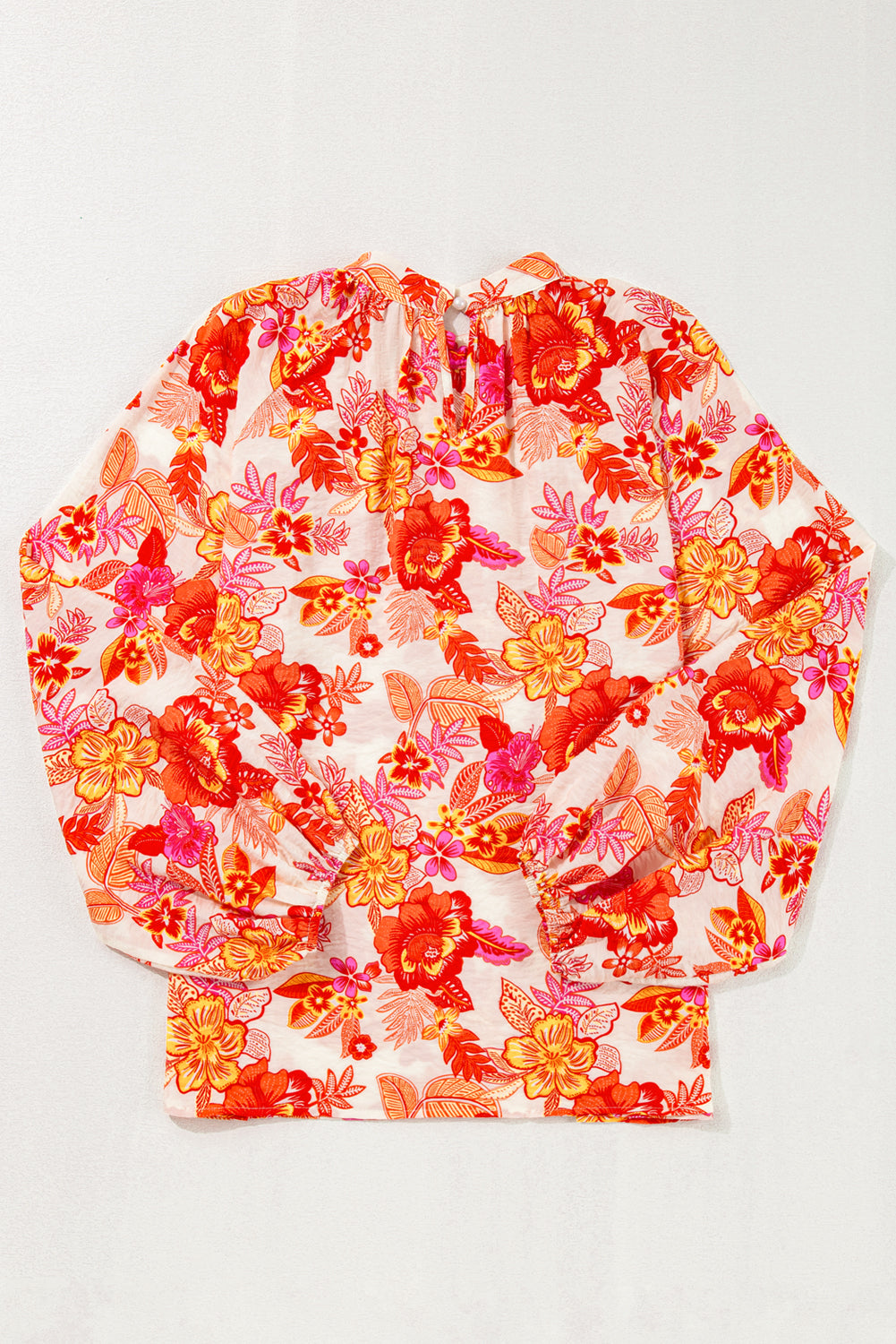 Blusa naranja con estampado floral, botones de perla, abertura tipo lágrima y manga larga abullonada.