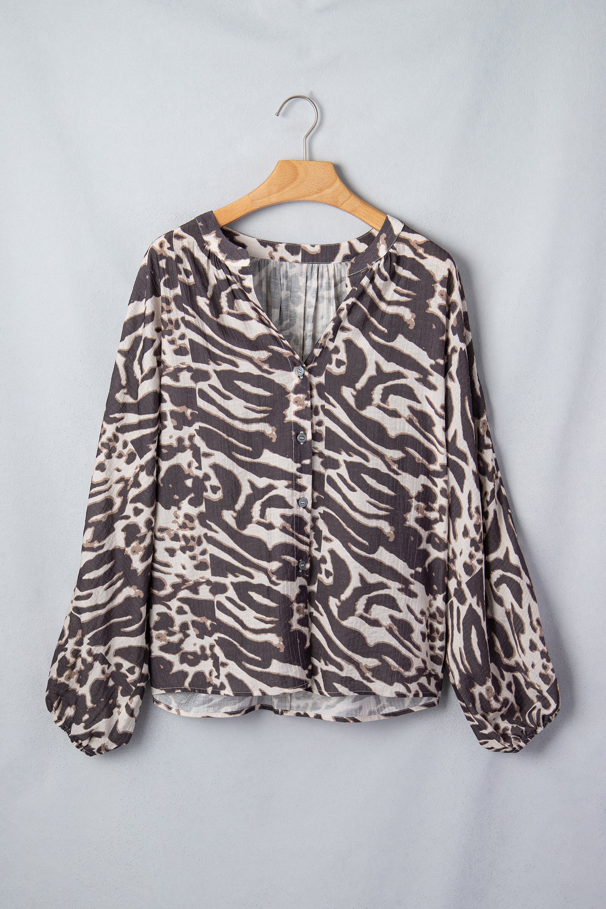 Camisa color pergamino con estampado de leopardo, cuello en V, cierre de botones y mangas abullonadas.