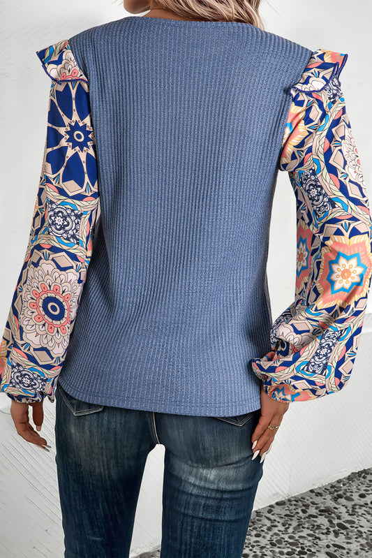 Blusa azul de punto tipo gofre con cuello redondo, diseño de paneles (patchwork), estampado floral y mangas con volantes.