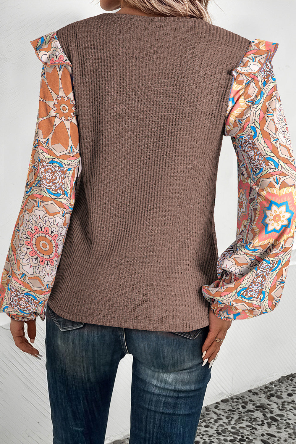 Blusa azul de punto tipo gofre con cuello redondo, diseño de paneles (patchwork), estampado floral y mangas con volantes.
