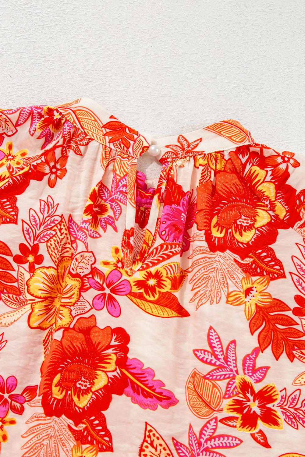 Blusa naranja con estampado floral, botones de perla, abertura tipo lágrima y manga larga abullonada.