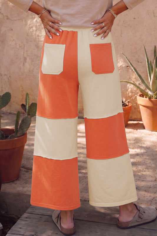 Pantalones casuales de pernera ancha y largo al tobillo, con diseño de bloques de color y costuras a la vista, en tono naranja rojizo.