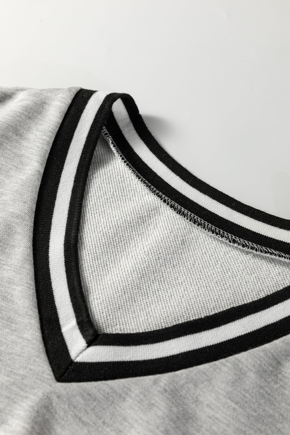 Vestido tipo camiseta de estilo preppy, manga larga y cuello en V, en gris claro con ribetes a rayas.