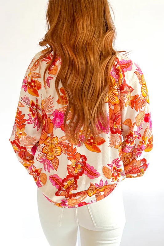 Blusa naranja con estampado floral, botones de perla, abertura tipo lágrima y manga larga abullonada.