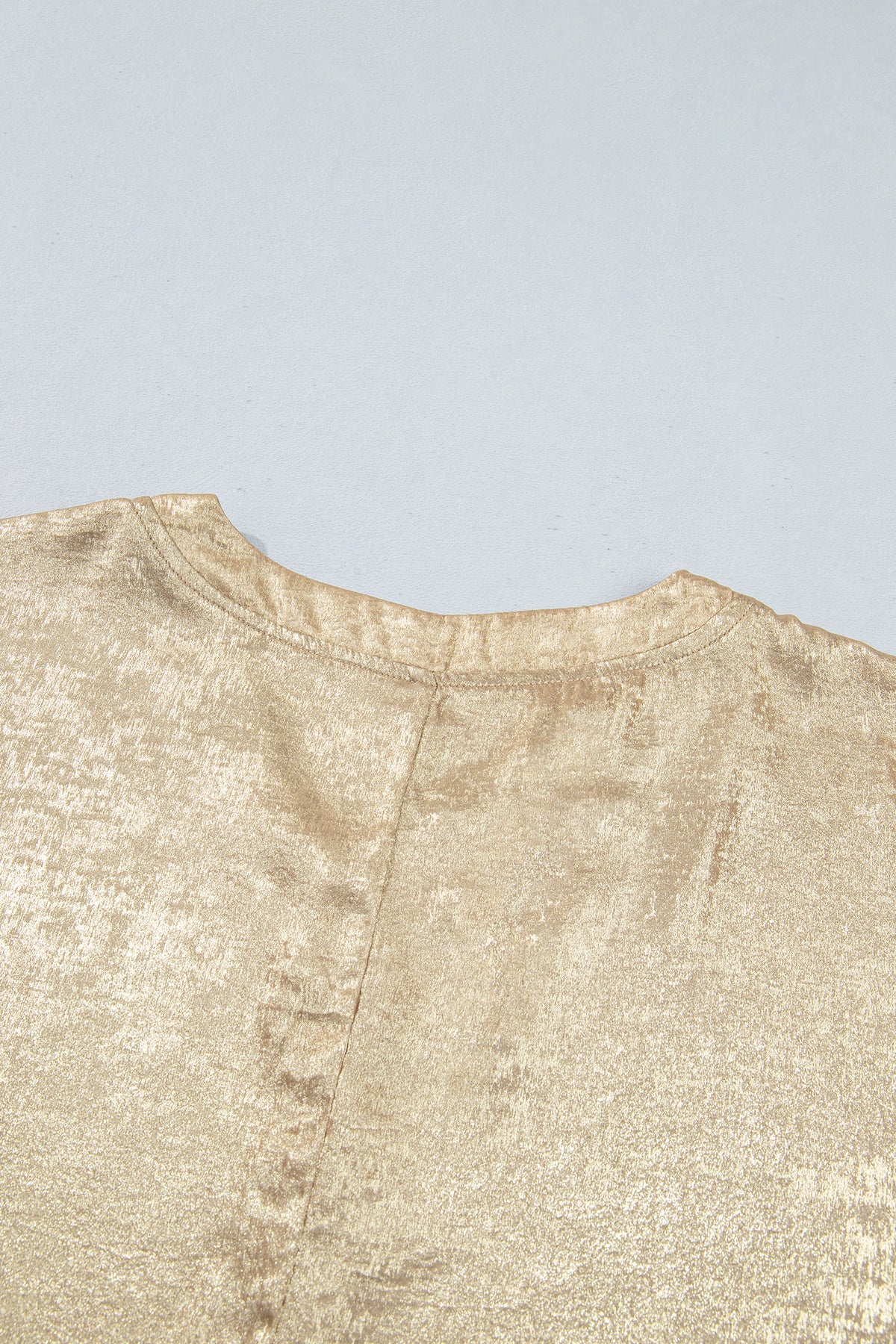 Blusa tipo dolman color pergamino metalizado con cuello en V, botones y puños en las mangas largas.