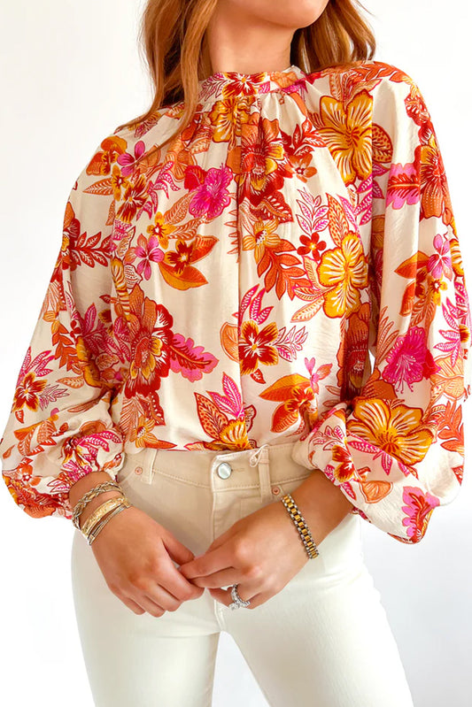 Blusa naranja con estampado floral, botones de perla, abertura tipo lágrima y manga larga abullonada.