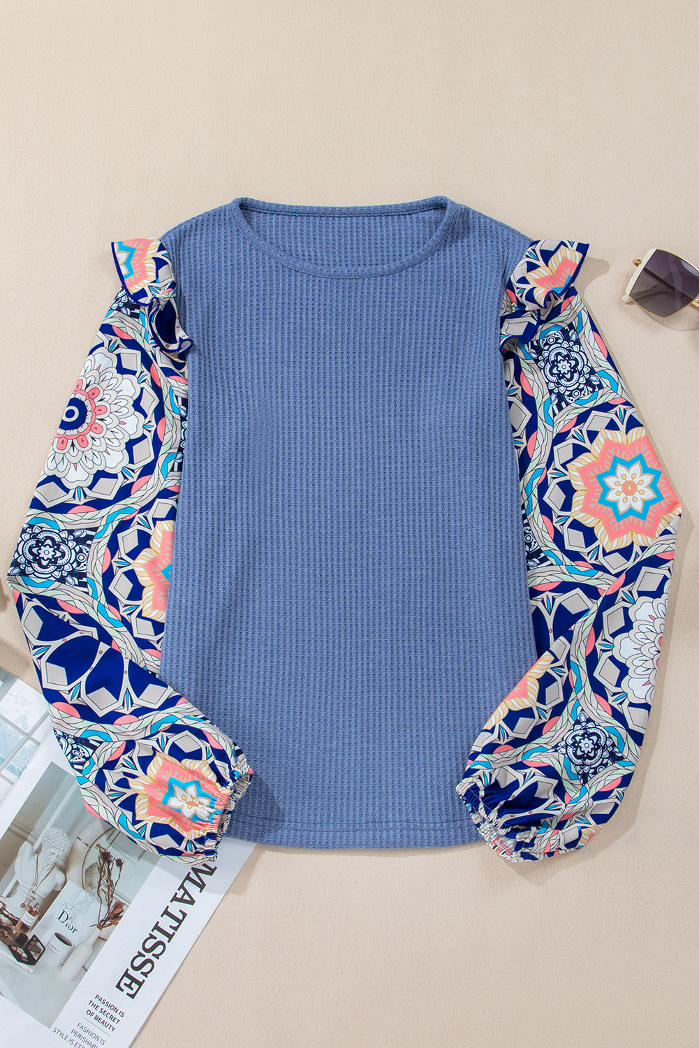 Blusa azul de punto tipo gofre con cuello redondo, diseño de paneles (patchwork), estampado floral y mangas con volantes.