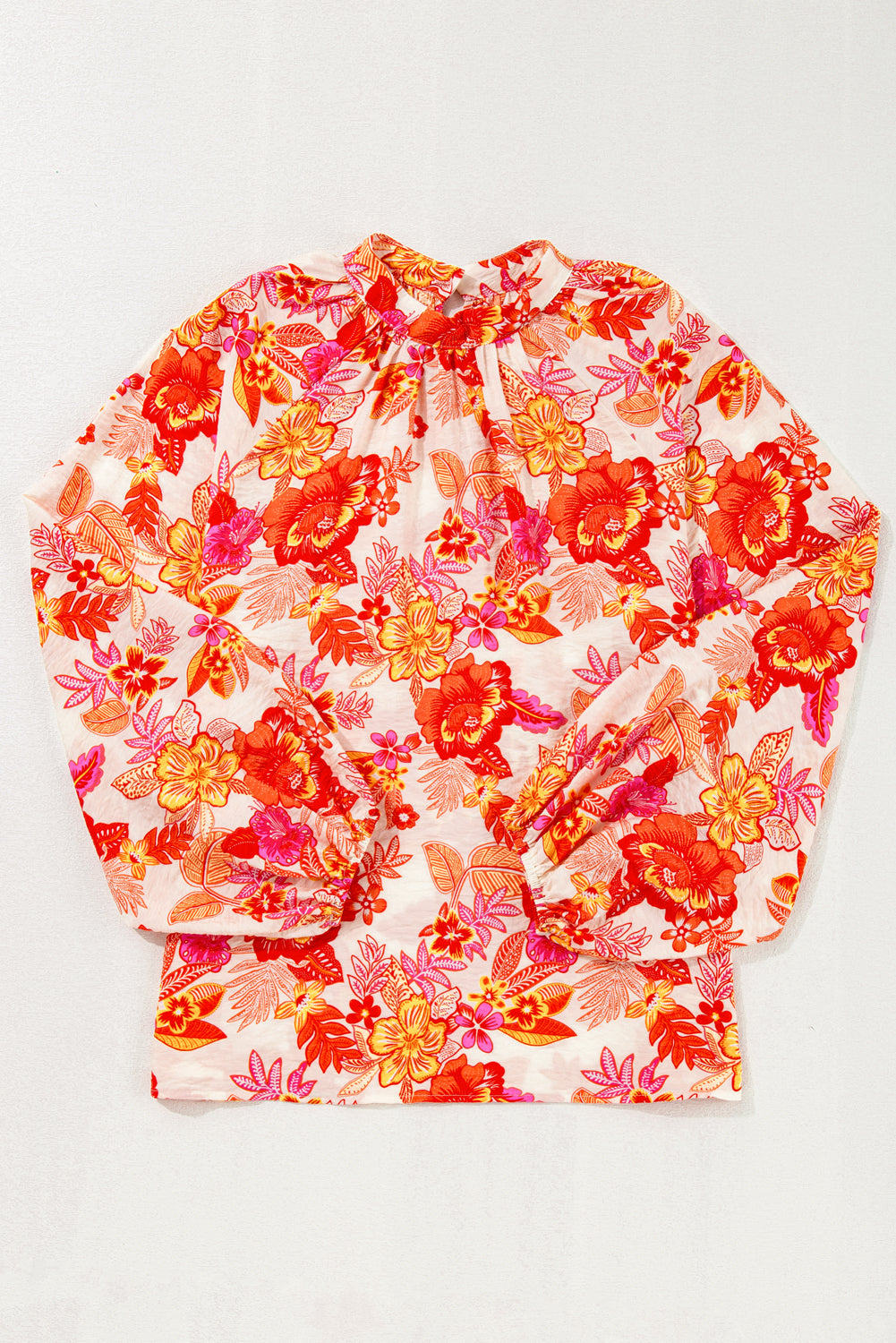 Blusa naranja con estampado floral, botones de perla, abertura tipo lágrima y manga larga abullonada.