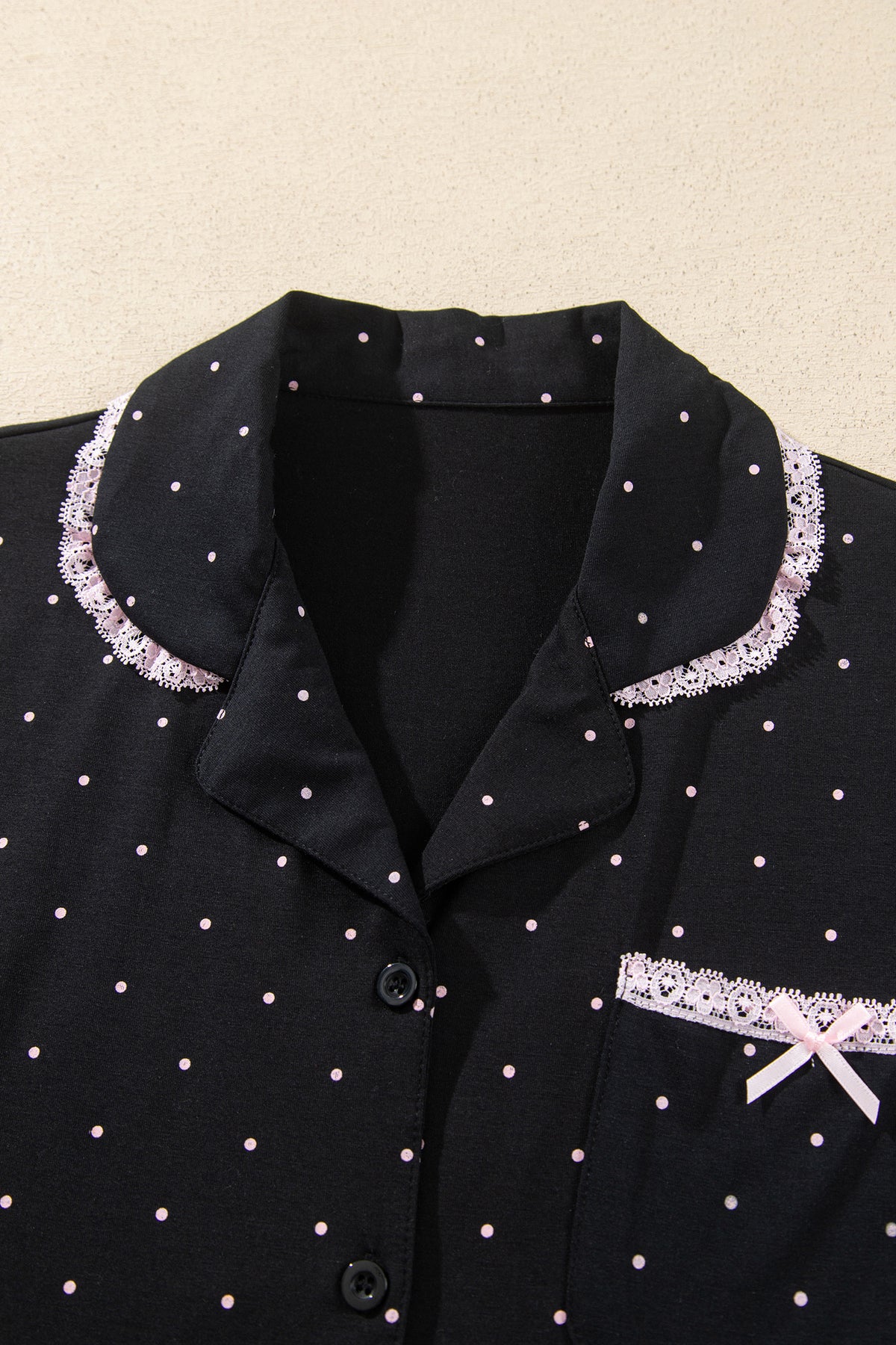 Conjunto de pijama de dos piezas: camisa de manga larga negra con lunares y detalles de encaje, y pantalón.