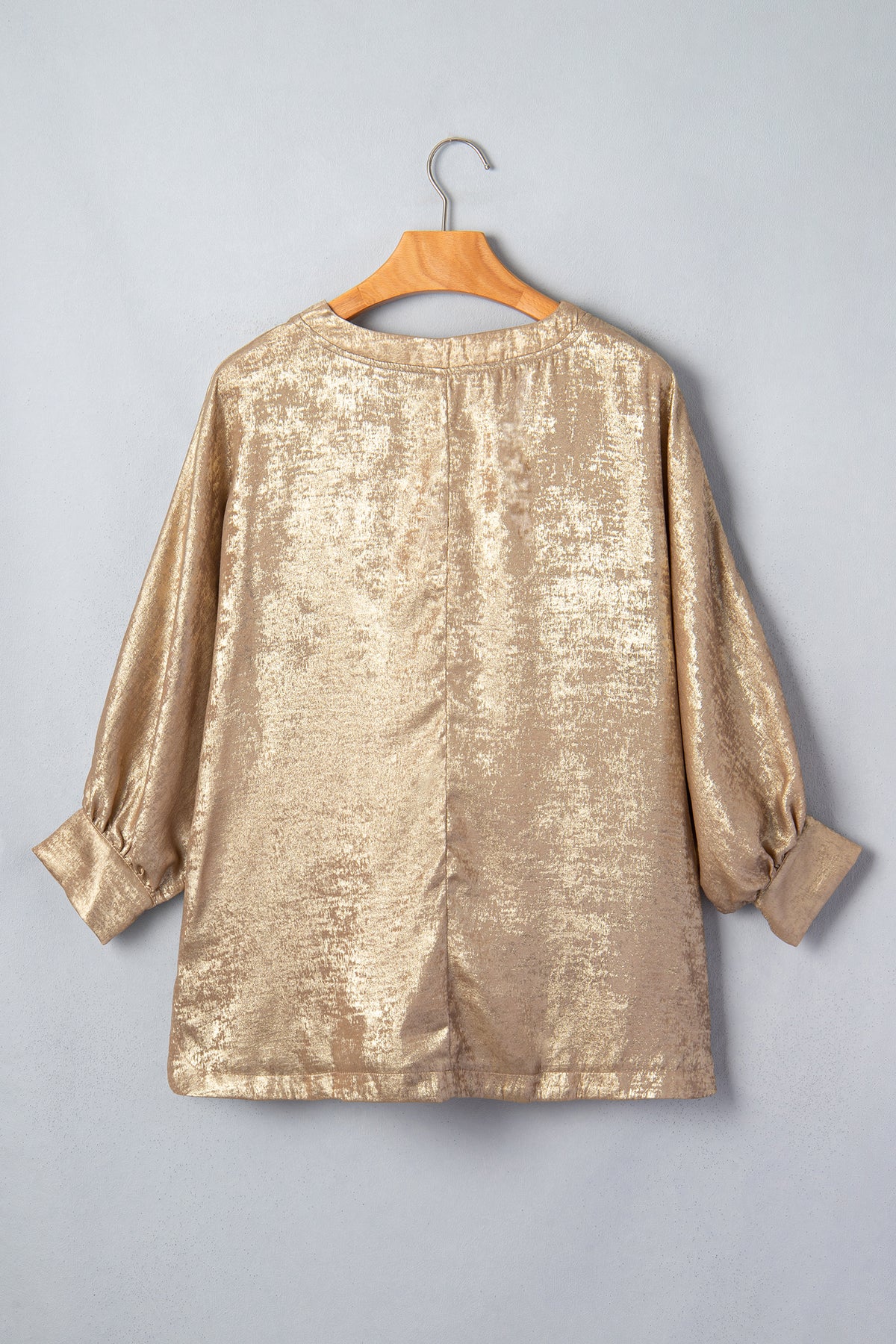 Blusa tipo dolman color pergamino metalizado con cuello en V, botones y puños en las mangas largas.