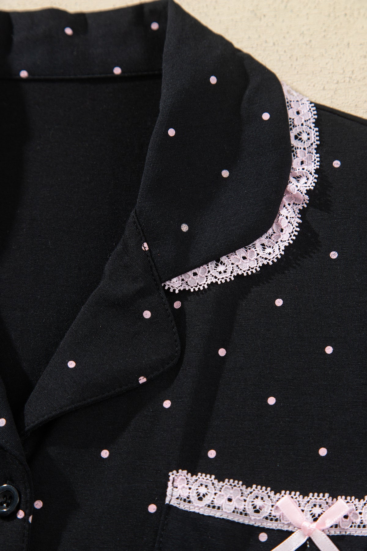 Conjunto de pijama de dos piezas: camisa de manga larga negra con lunares y detalles de encaje, y pantalón.