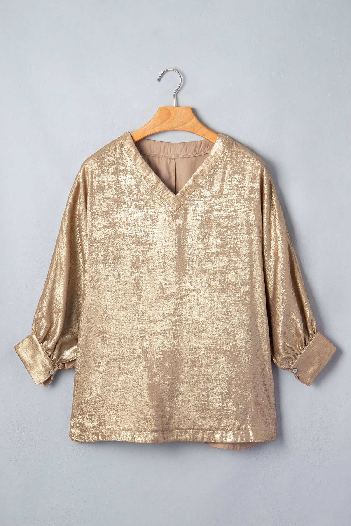 Blusa tipo dolman color pergamino metalizado con cuello en V, botones y puños en las mangas largas.