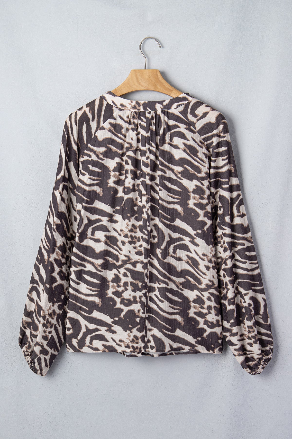 Camisa color pergamino con estampado de leopardo, cuello en V, cierre de botones y mangas abullonadas.