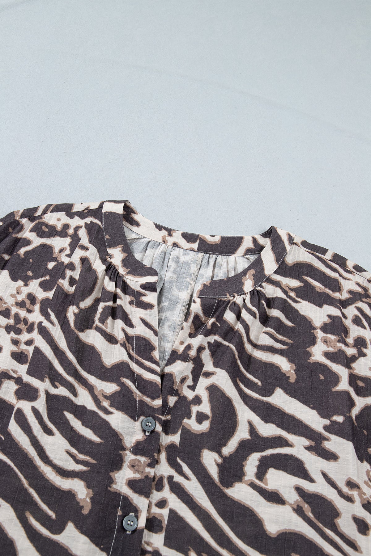 Camisa color pergamino con estampado de leopardo, cuello en V, cierre de botones y mangas abullonadas.