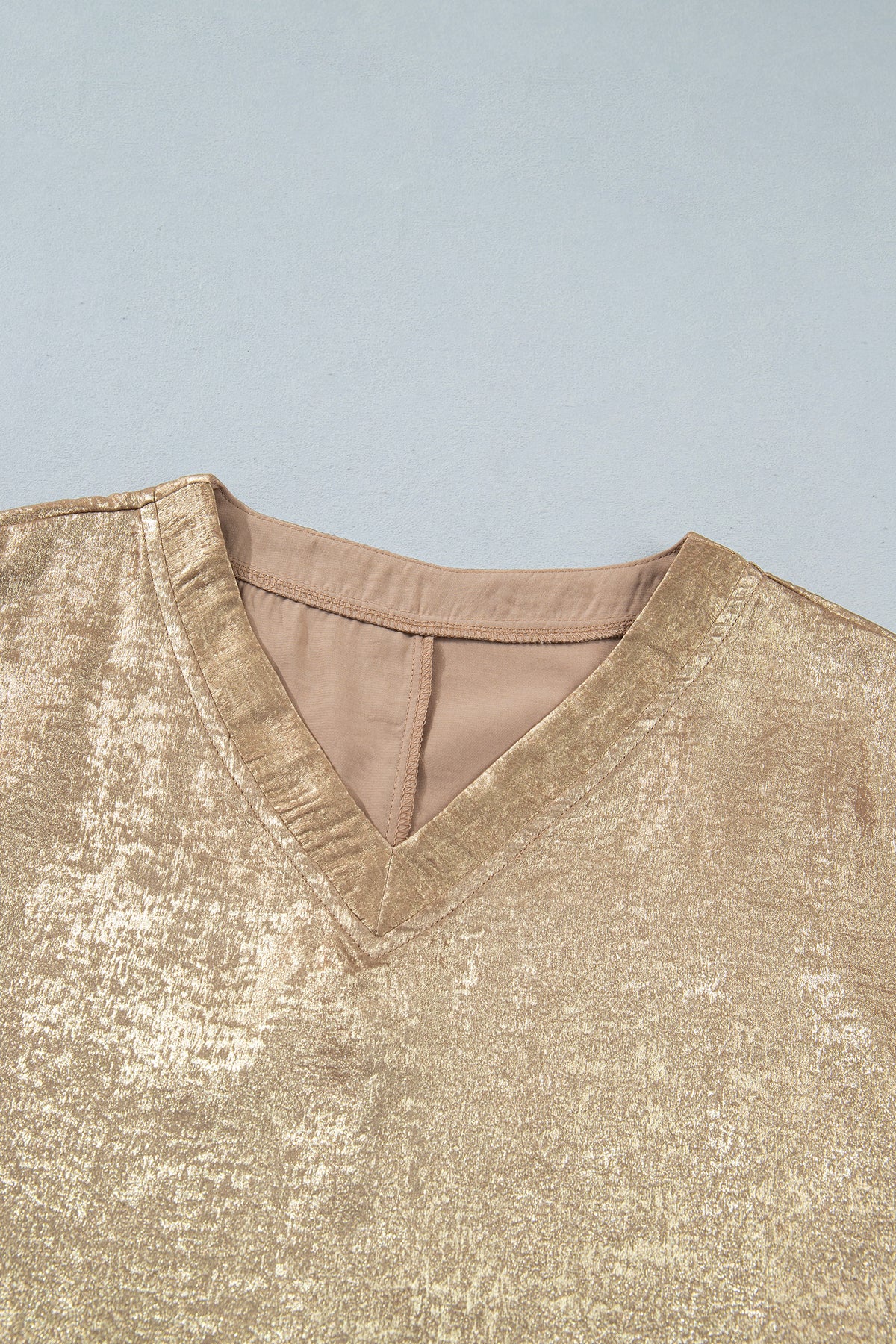Blusa tipo dolman color pergamino metalizado con cuello en V, botones y puños en las mangas largas.